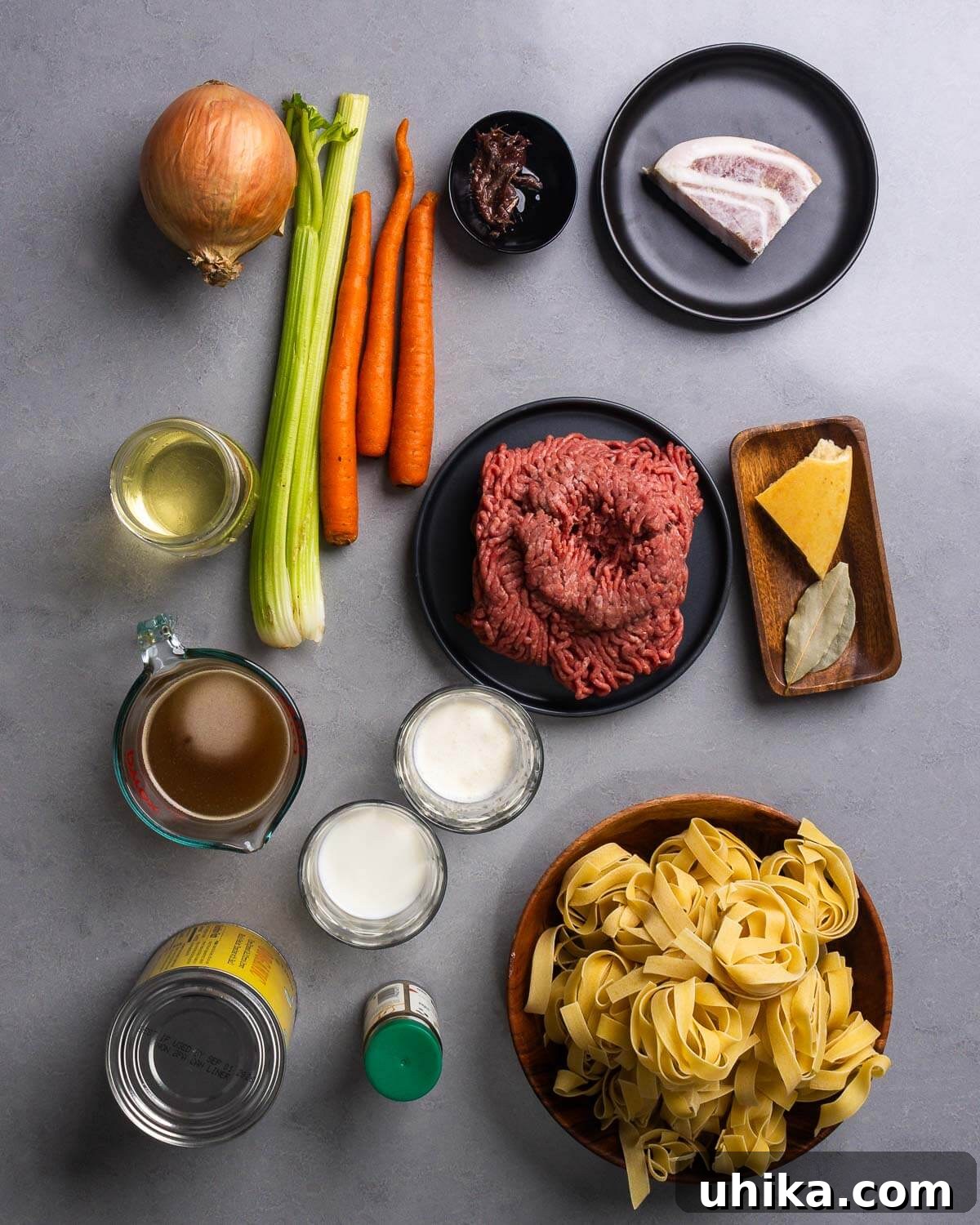 Pappardelle Bolognese An Elevated Classic 4 A beautifully arranged flat lay of all the essential ingredients for Pappardelle Bolognese: fresh onion, celery, carrots, tiny anchovy fillets, savory pancetta, a bottle of white wine, rich ground chuck, a parmesan rind, aromatic bay leaves, hearty beef stock, creamy milk and cream, vibrant canned tomatoes, a sprinkle of nutmeg, and delicate pappardelle nests.
