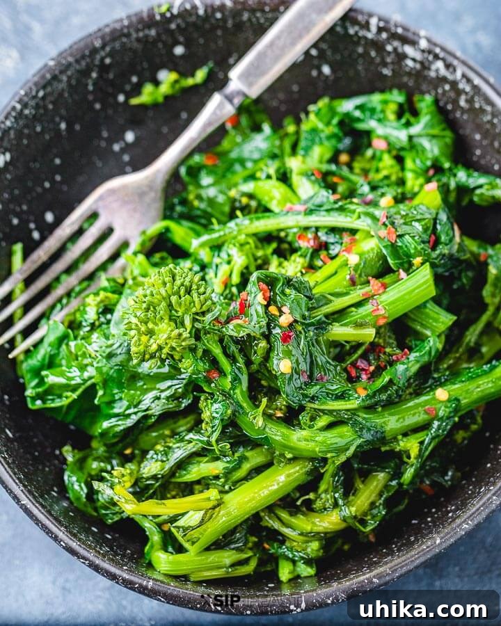 Serving Sauteed Broccoli Rabe - Sip & Feast #italianfoodphotography #healthyrecipes #mediterraneanvegetables A black bowl brimming with freshly sauteed broccoli rabe, elegantly placed on a blue wooden surface, ready to be enjoyed.