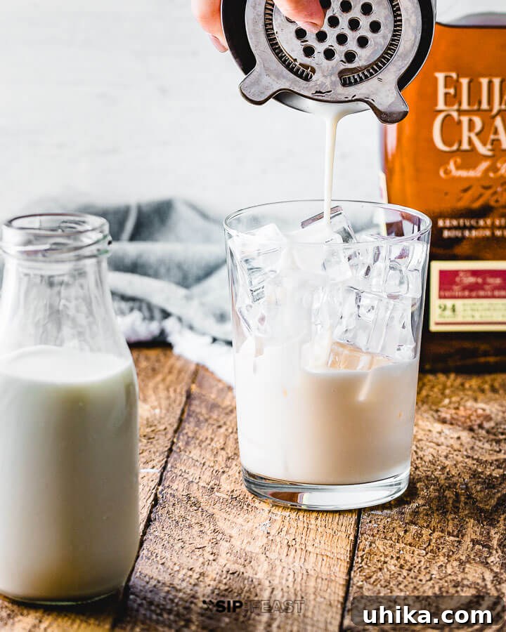 Pumpkin Spice Bourbon Velvet Punch 5 Pouring the milk punch mixture into a glass filled with ice.
