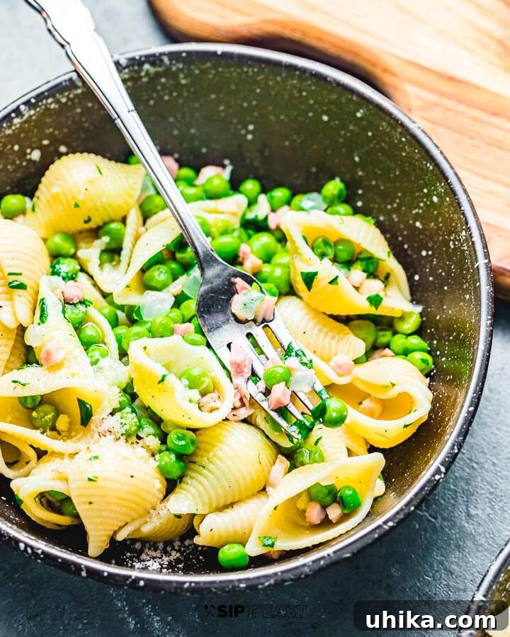 A black bowl filled with perfectly cooked shell pasta, crispy pancetta, and vibrant green peas, ready to be enjoyed.
