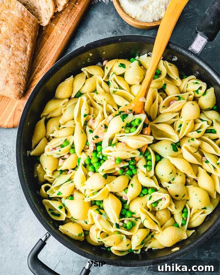 Large deep pan filled with hot shell pasta, crispy pancetta, and vibrant green peas, resting on a blue kitchen cloth.