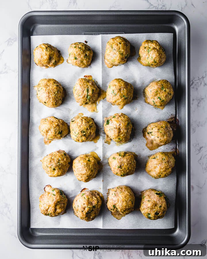 Fully cooked meatballs on parchment paper lined pan.