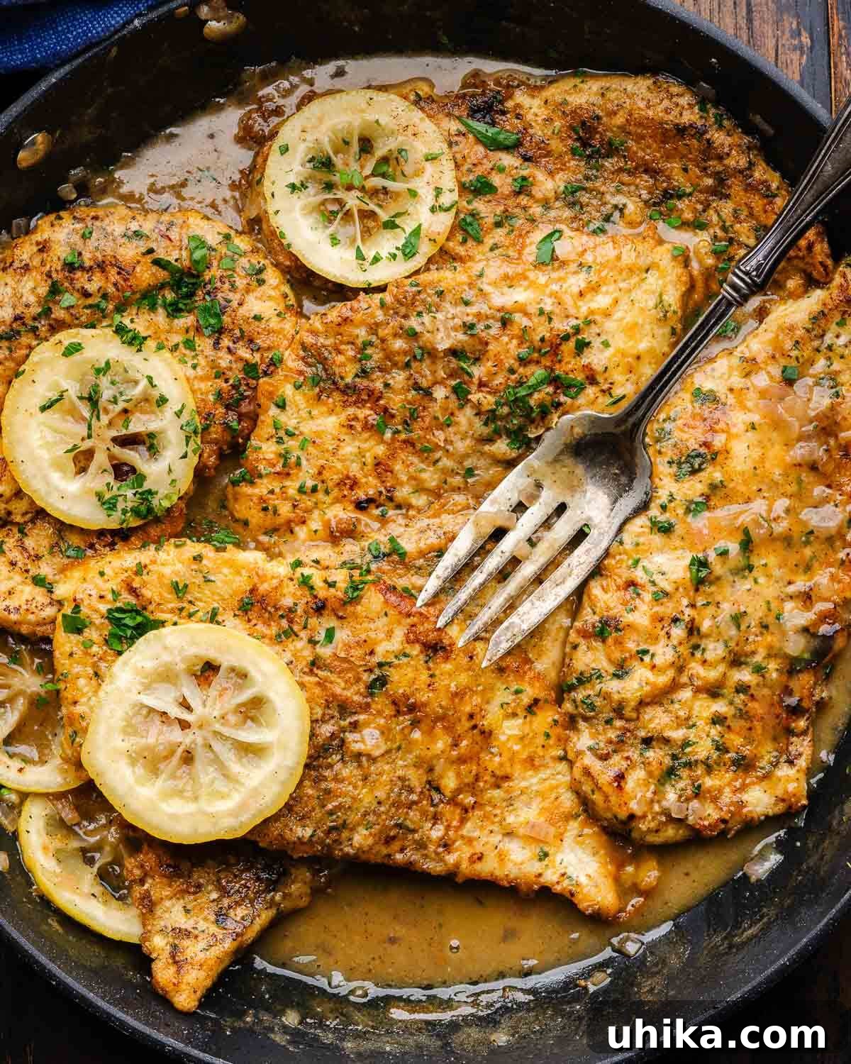 Golden Chicken Francese with Zesty Lemon Butter 2 Chicken Francese in black pan with lemon slices.