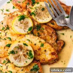 Chicken Francese in white platter with lemon slices and large serving fork.