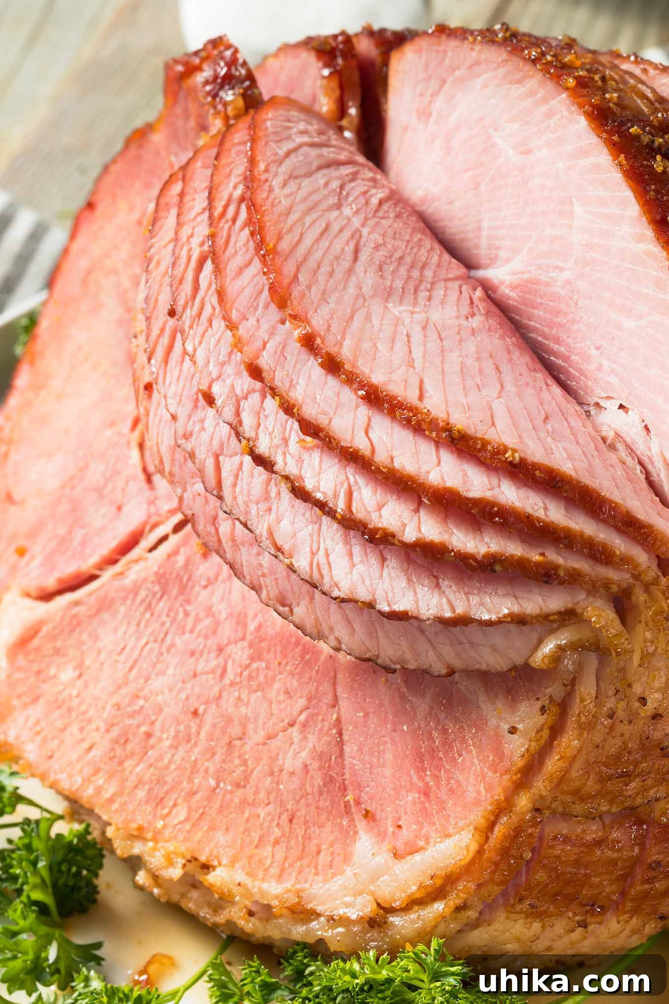 Unlock the Secret to a Perfectly Glazed Ham 2 Close-up of a glazed, spiral-sliced ham on a platter with the first few slices falling forward, ready for serving.