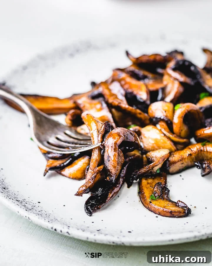 Sauteed Balsamic Portobello Mushrooms - sipandfeast.com #sidedish #italianfood #mushrooms A white plate filled with glistening sauteed balsamic portobello mushrooms, garnished with fresh parsley, alongside a fork.