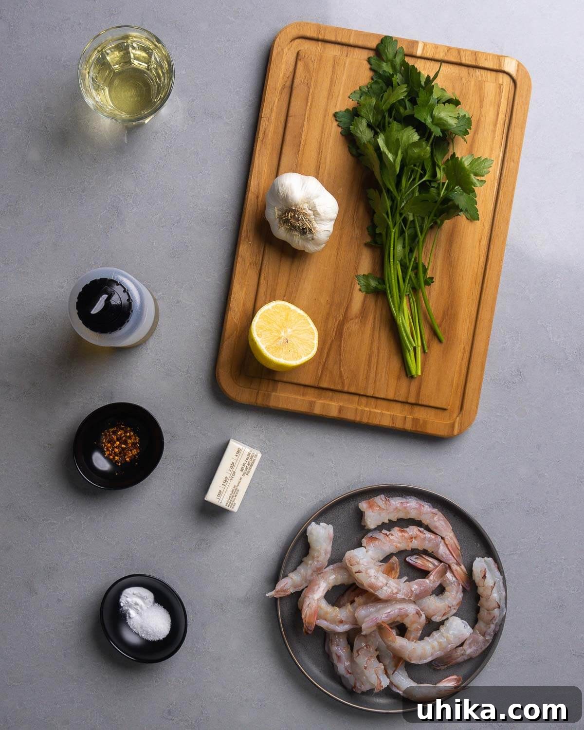 Effortless Garlic Shrimp Delight 3 A flat lay of fresh ingredients for shrimp scampi including white wine, olive oil, garlic, lemon, parsley, hot red pepper flakes, butter, salt, baking soda, and raw shrimp.