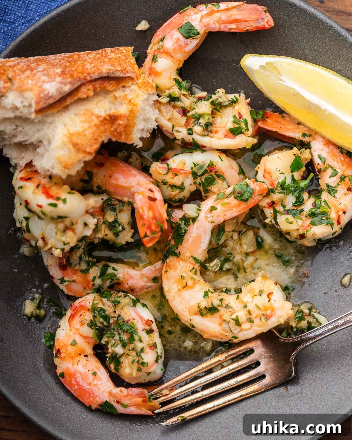 Effortless Garlic Shrimp Delight 7 A serving of shrimp scampi in a grey plate, garnished with a lemon wedge and fresh parsley, with crusty Italian bread on the side.