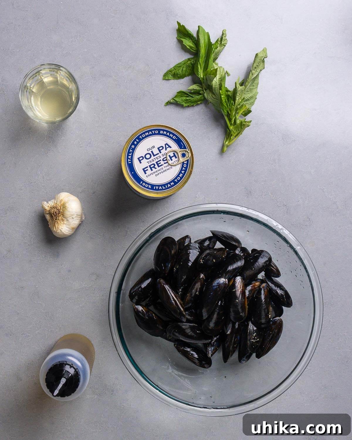 Marinara Mussels in Minutes: Easy Seafood Appetizer 4 A flat lay showing fresh ingredients for Mussels Marinara: white wine, canned plum tomatoes, fresh basil, garlic cloves, olive oil, and raw mussels.