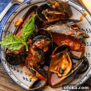 Mussels marinara in white bowl with basil garnish.