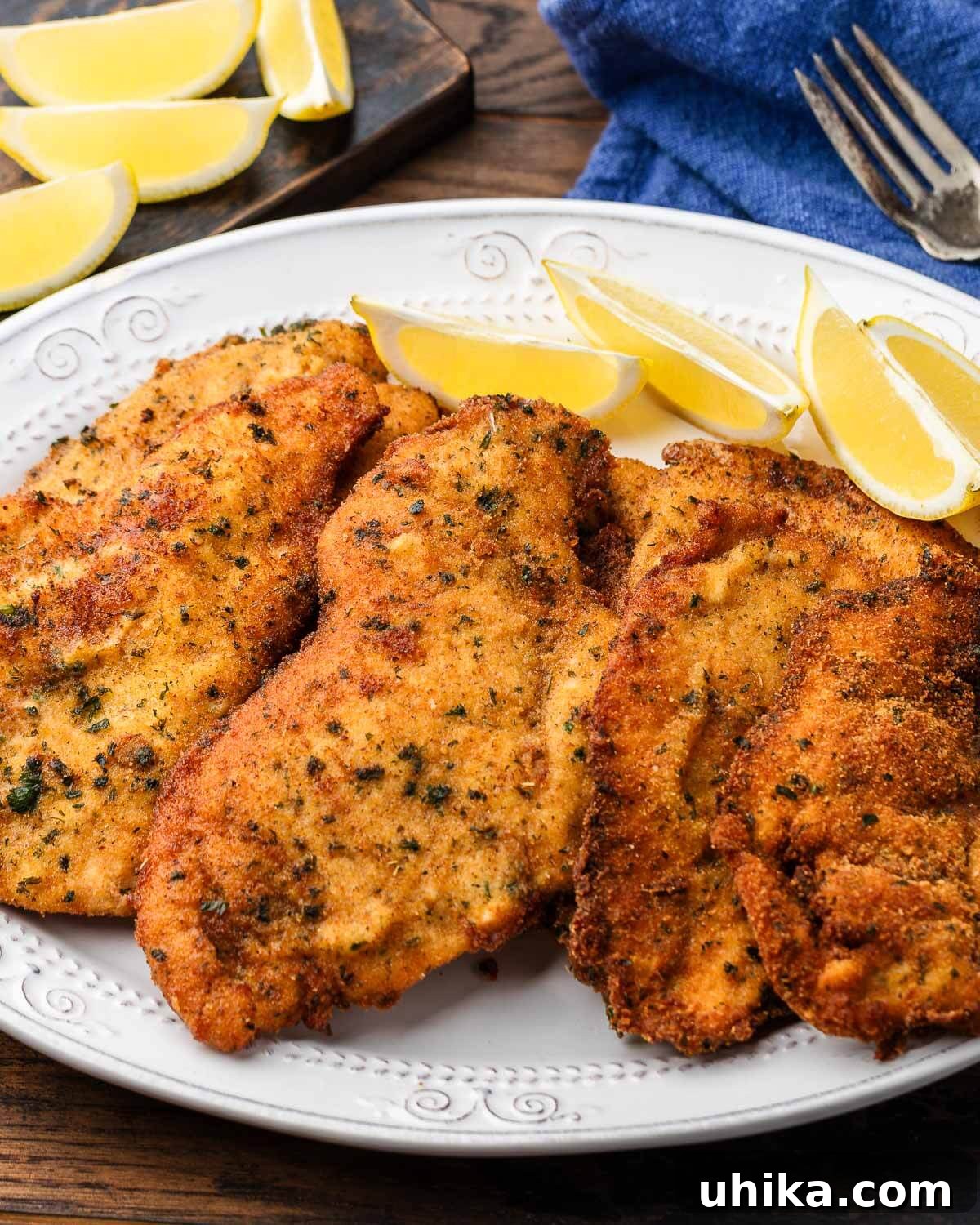 Crispy Italian Chicken Cutlets 2 Italian chicken cutlets on white platter with lemon wedges, beautifully golden and crispy.