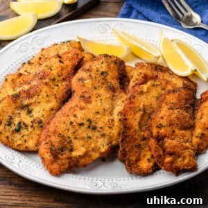 Crispy Italian Chicken Cutlets 7 Italian chicken cutlets on white platter with lemon wedges.