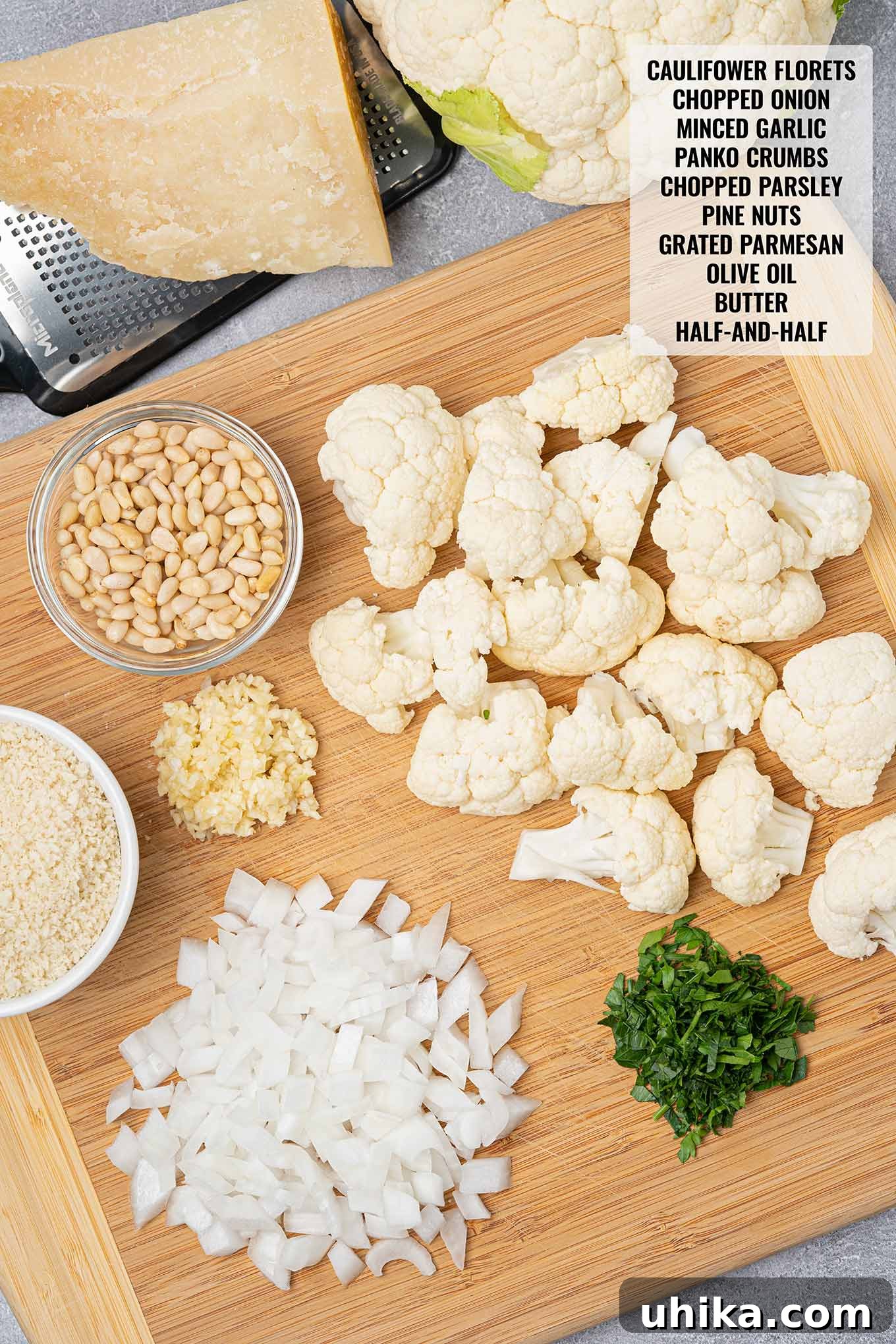 Recipe ingredients on a cutting board including cauliflower florets, onion, garlic, pine nuts, panko, parsley, and cheese.
