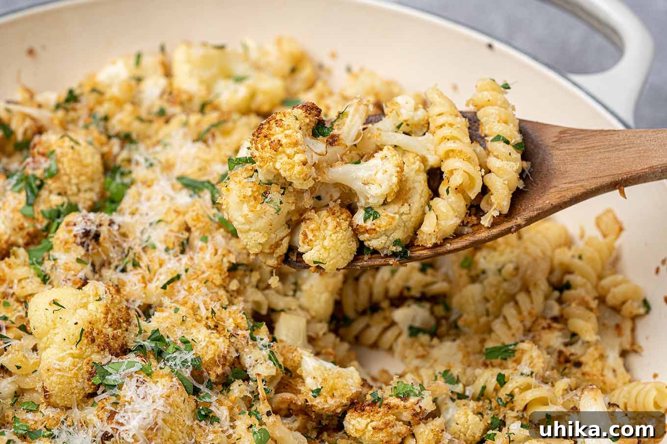 Roasted cauliflower combined with rotini, cheese, toasted breadcrumbs, and pine nuts being served from the pan.