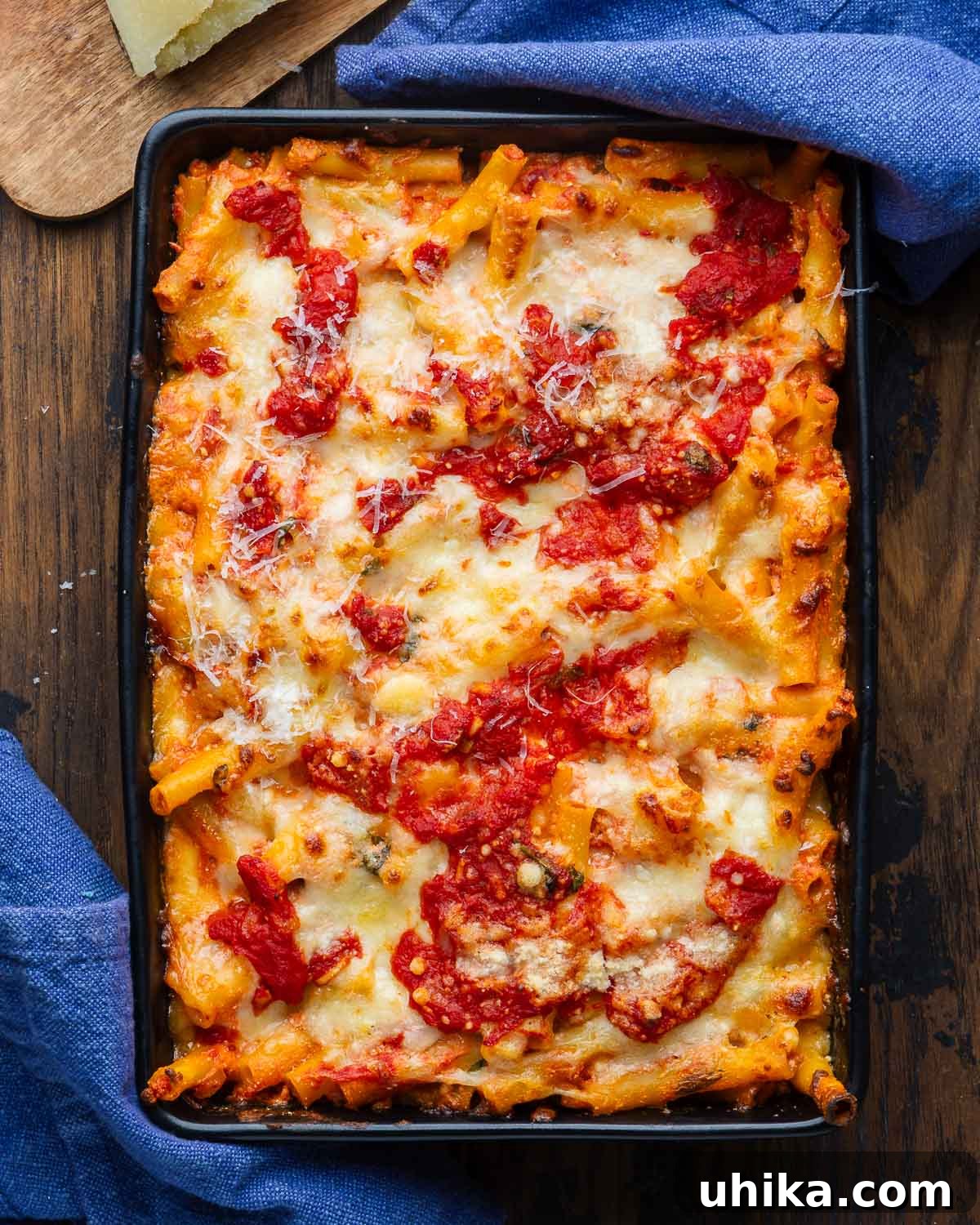 Baked ziti in black baking dish with blue napkins. A classic Italian-American comfort food dish, ready to be served.