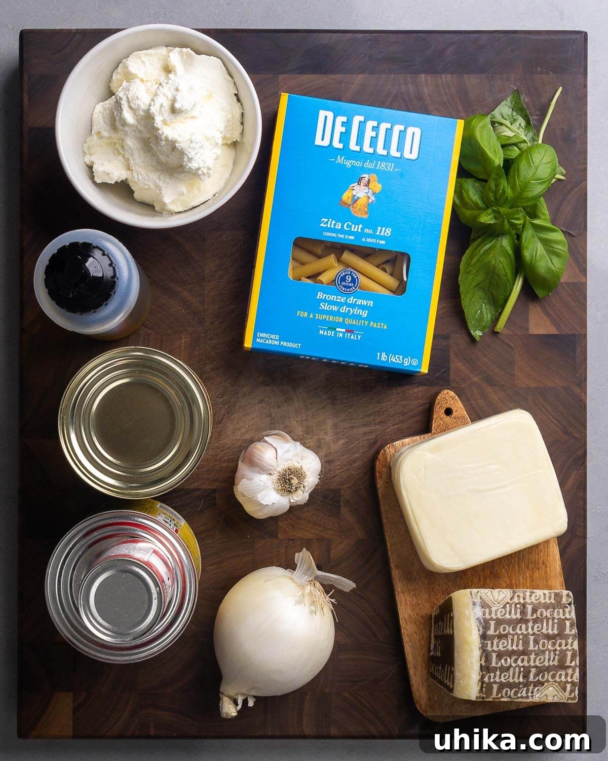 Ingredients shown: creamy ricotta cheese, tubular ziti pasta, fresh basil, high-quality olive oil, canned plum tomatoes, concentrated tomato paste, minced garlic, diced onion, block mozzarella, and grated Pecorino Romano cheese.
