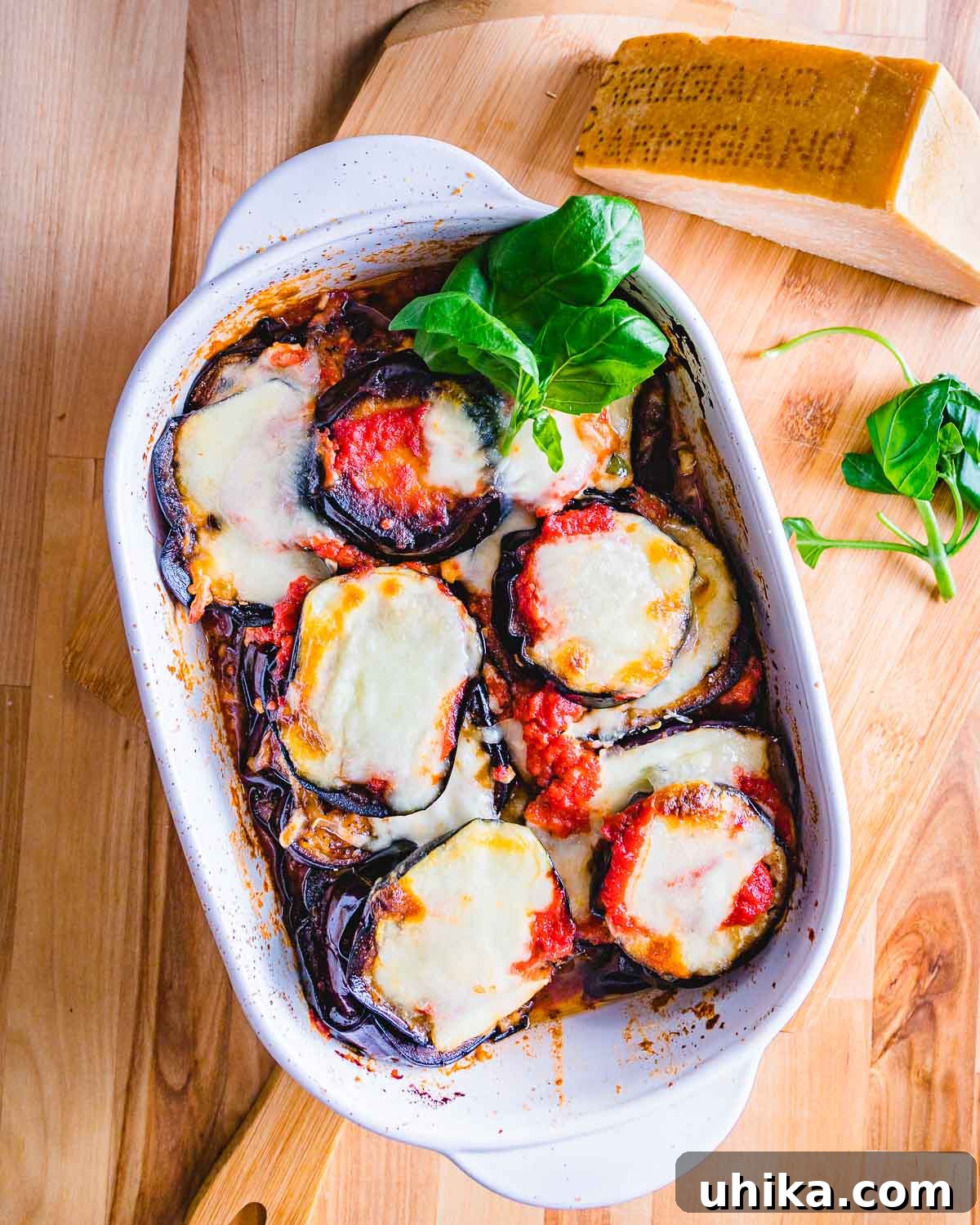 Gluten-Free Eggplant Parmigiana 2 Overhead shot of a large dish with finished eggplant parmesan and a block of Parmigiano Reggiano cheese, showcasing the golden-brown top and melted cheese.