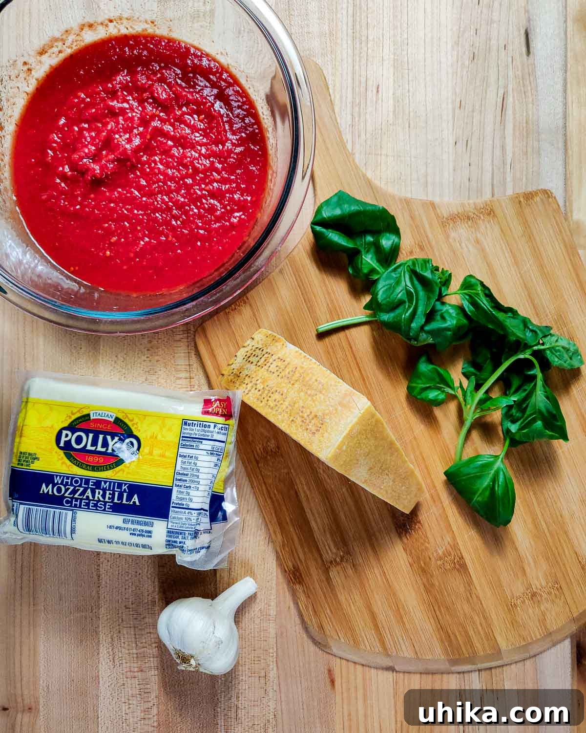 Gluten-Free Eggplant Parmigiana 3 Ingredients for Sicilian-style eggplant parmigiana laid out: rich marinara sauce, fresh basil leaves, a block of Parmigiano Reggiano, shredded mozzarella, and aromatic garlic cloves.