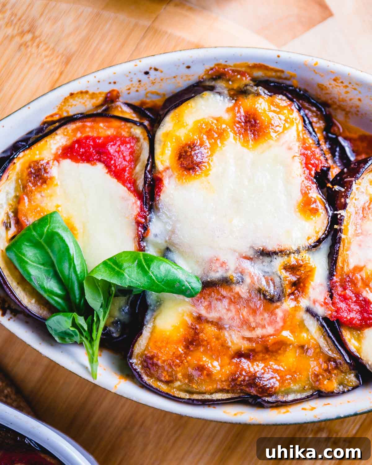 Gluten-Free Eggplant Parmigiana 5 Eggplant parmigiana served in a small oval-shaped bowl, garnished with fresh basil.
