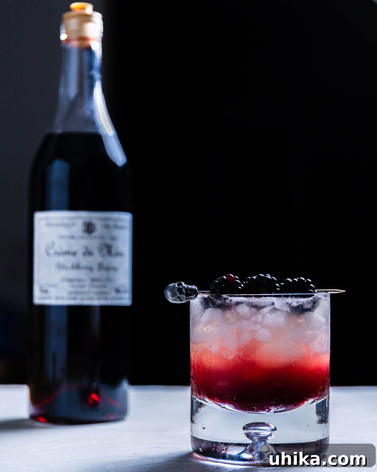 Blackberry Bramble - sipandfeast.com #bramble #drinks #cocktails A beautifully presented Blackberry Bramble cocktail in a rocks glass, garnished with three fresh blackberries on a skewer, showcasing its rich purple color.