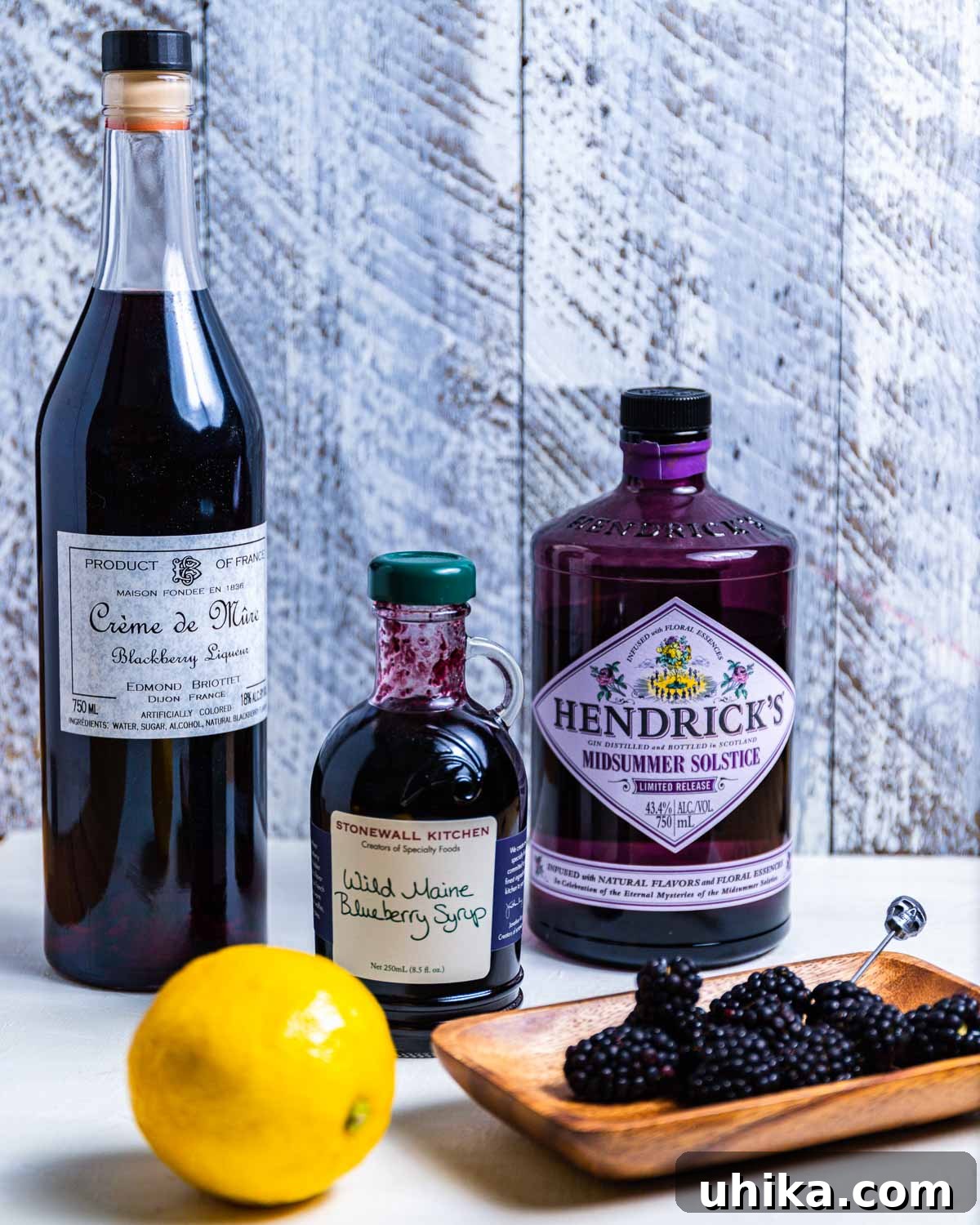 Blackberry Bramble - sipandfeast.com #bramble #drinks #cocktails All the ingredients for a Blackberry Bramble laid out: a bottle of crème de mûre, blueberry syrup, gin, fresh lemons, and a plate of ripe blackberries.