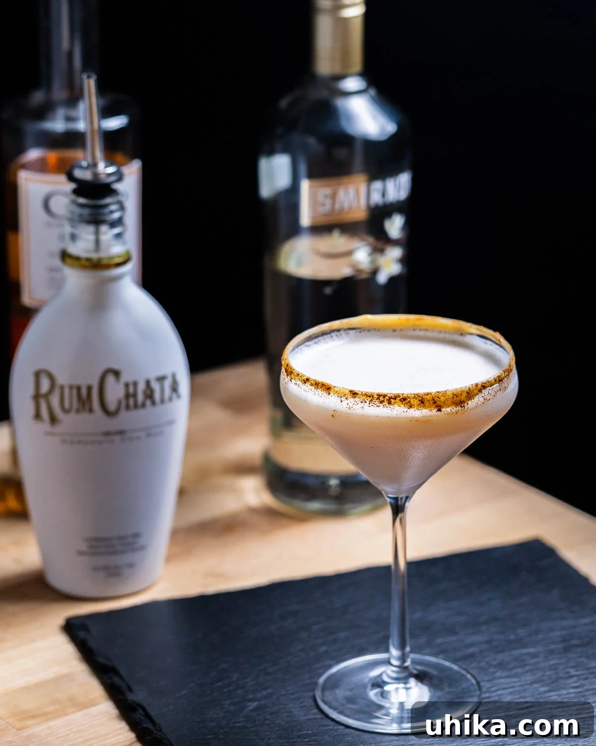 Autumn Spiced Martini 2 A beautifully presented Pumpkin Spice Martini in a chilled martini glass, with bottles of RumChata and vanilla vodka subtly in the background on a rustic wooden table.