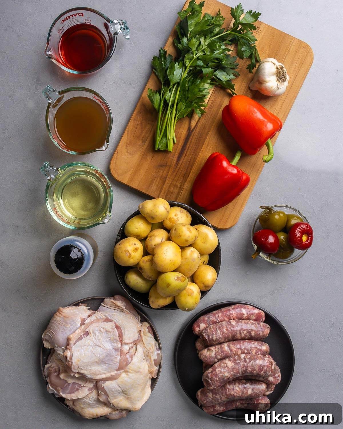 Rustic Italian Chicken and Sausage Skillet 3 A beautifully arranged selection of fresh ingredients for Chicken Scarpariello, including red wine vinegar, chicken stock, white wine, olive oil, fresh parsley, garlic cloves, red bell peppers, small potatoes, hot cherry peppers, bone-in chicken thighs, and raw Italian sausage links.