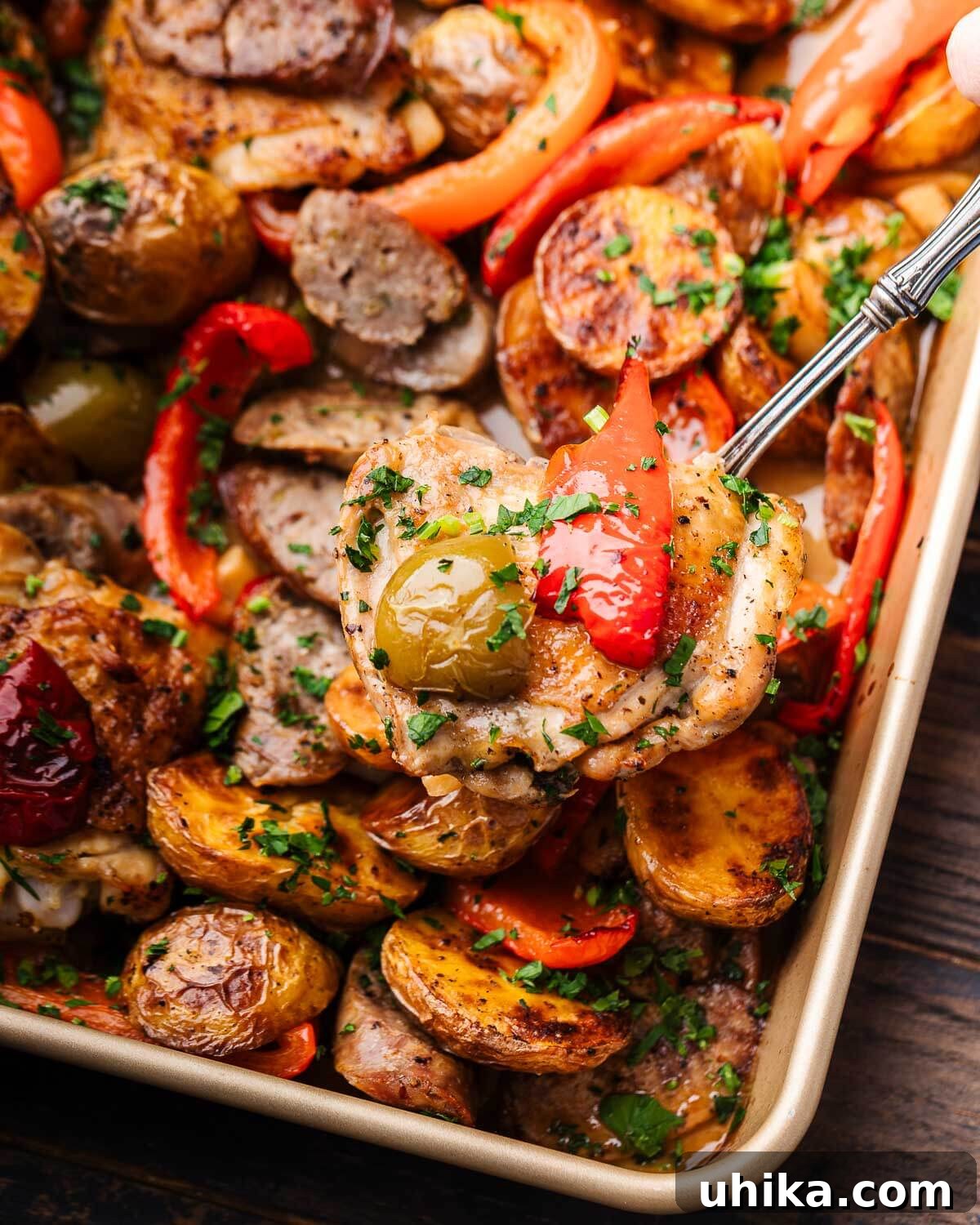 Rustic Italian Chicken and Sausage Skillet 7 A hand holding a serving fork with a piece of crispy chicken thigh, hovering over a baking pan filled with Chicken Scarpariello.