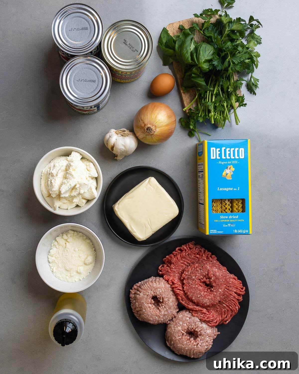 Old-World Comfort: Italian-American Lasagna 4 Ingredients shown: 3 cans of plum tomatoes, egg, basil, parsley, onion, garlic, ricotta, mozzarella, lasagna noodles, pecorino romano, olive oil, ground beef, and ground pork.