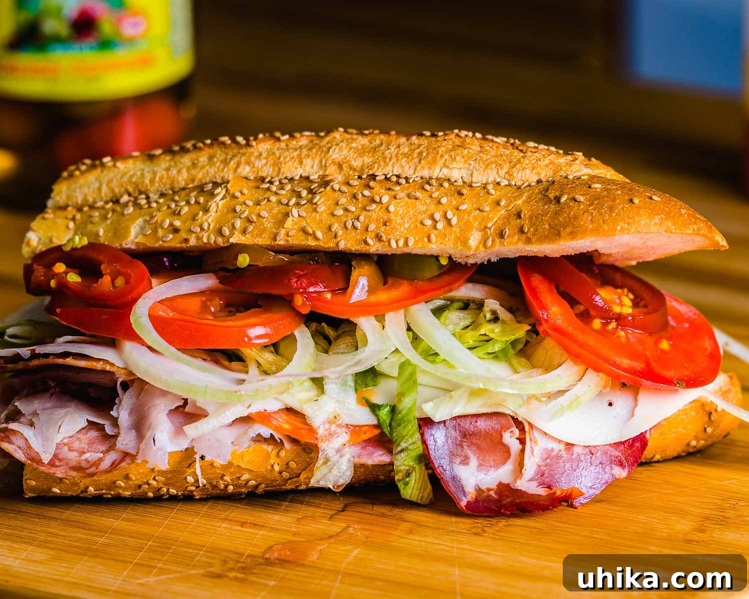 Italian sub on seeded roll with lettuce, tomato, cherry peppers, and onions showing.