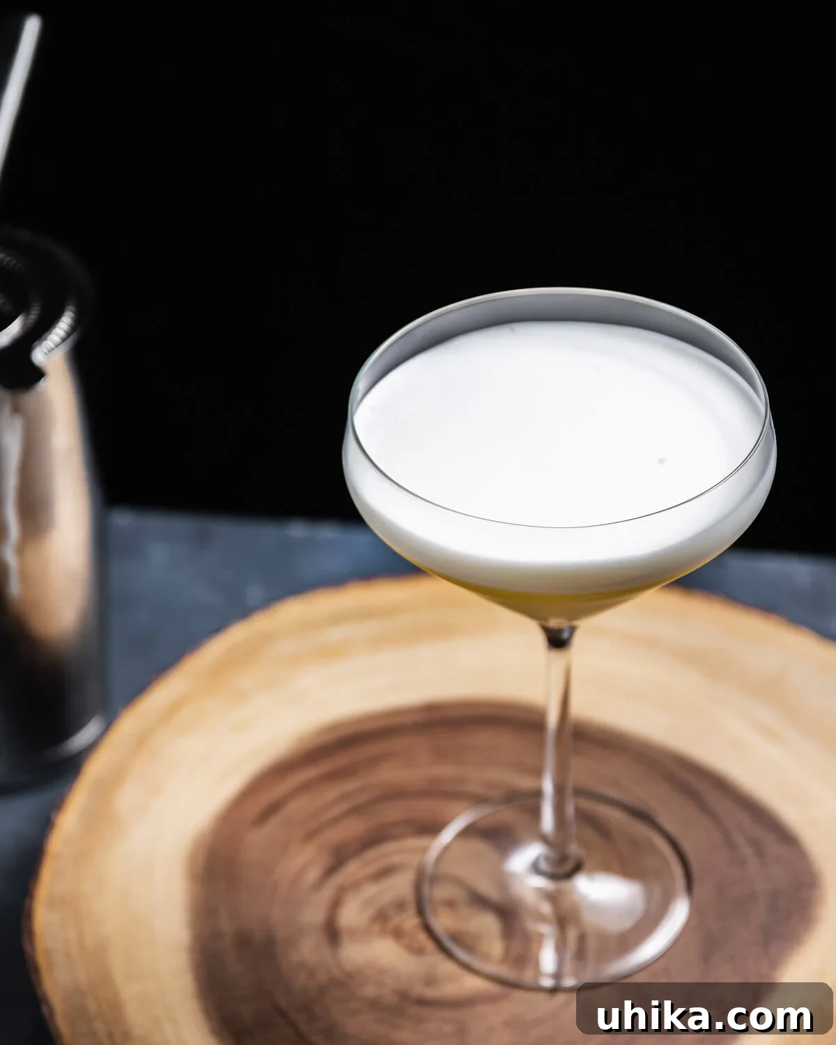 Cocktail in coupe glass on round wooden board, with elegant foam.