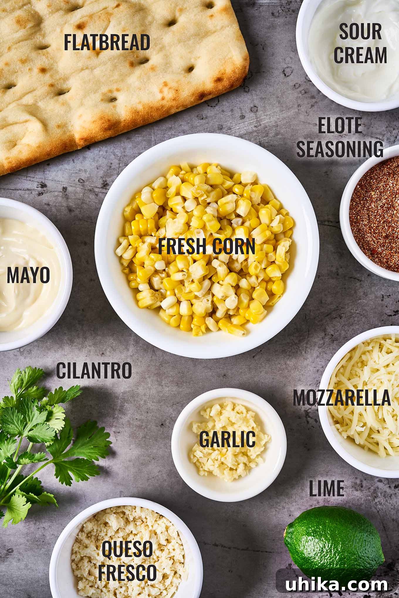Elote Flatbread Fiesta 3 A beautifully arranged overhead shot showcasing all the fresh ingredients needed for Mexican street corn flatbread, including plump corn kernels, ready-to-use flatbreads, aromatic elote seasoning, crumbled queso fresco, vibrant lime wedges, and fresh cilantro sprigs.