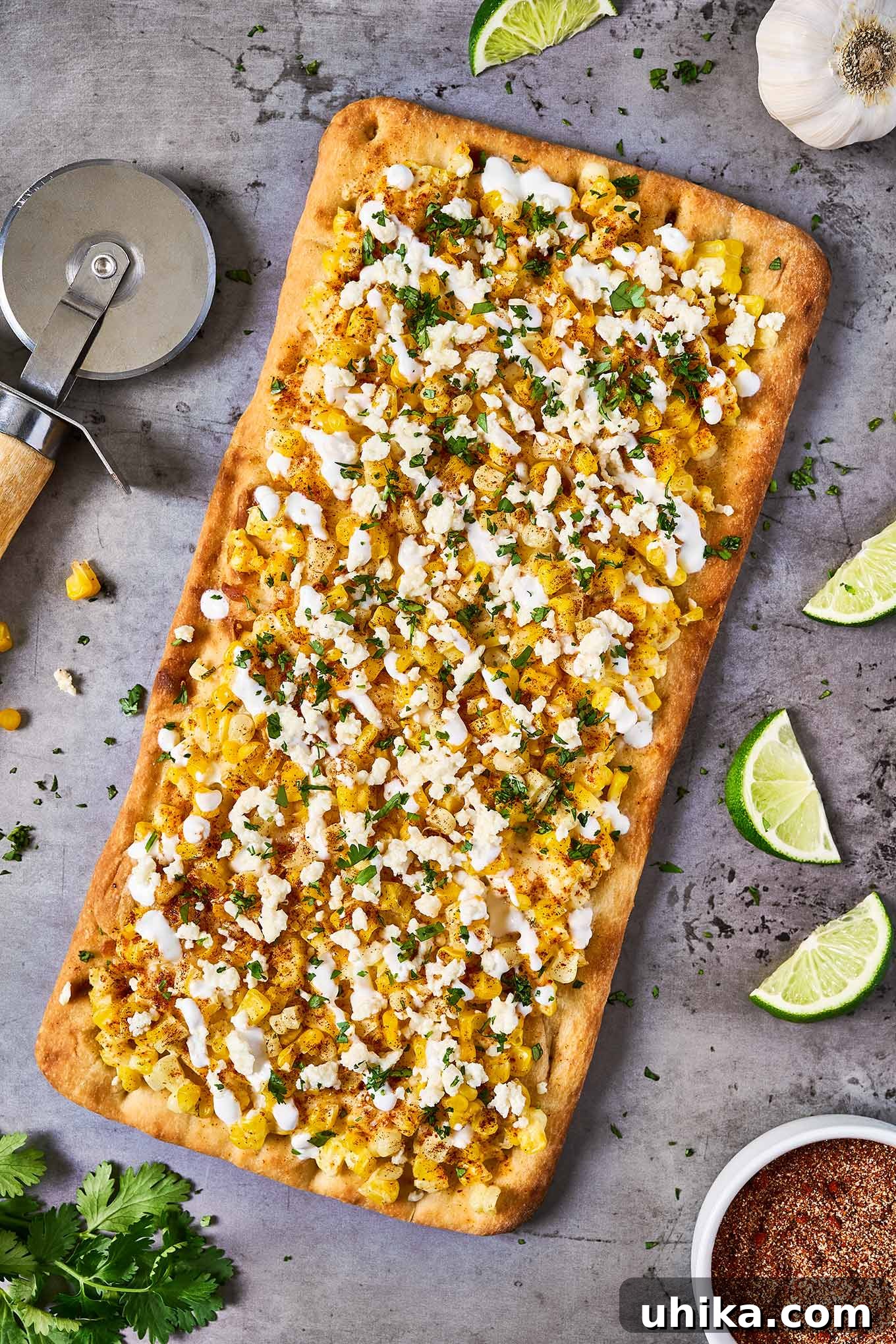 Elote Flatbread Fiesta 4 A delicious flatbread being prepared on a baking sheet, generously topped with melted mozzarella cheese, golden corn kernels, crumbled queso fresco, freshly chopped cilantro, a sprinkle of aromatic seasoning blend, and a delicate drizzle of creamy crema.