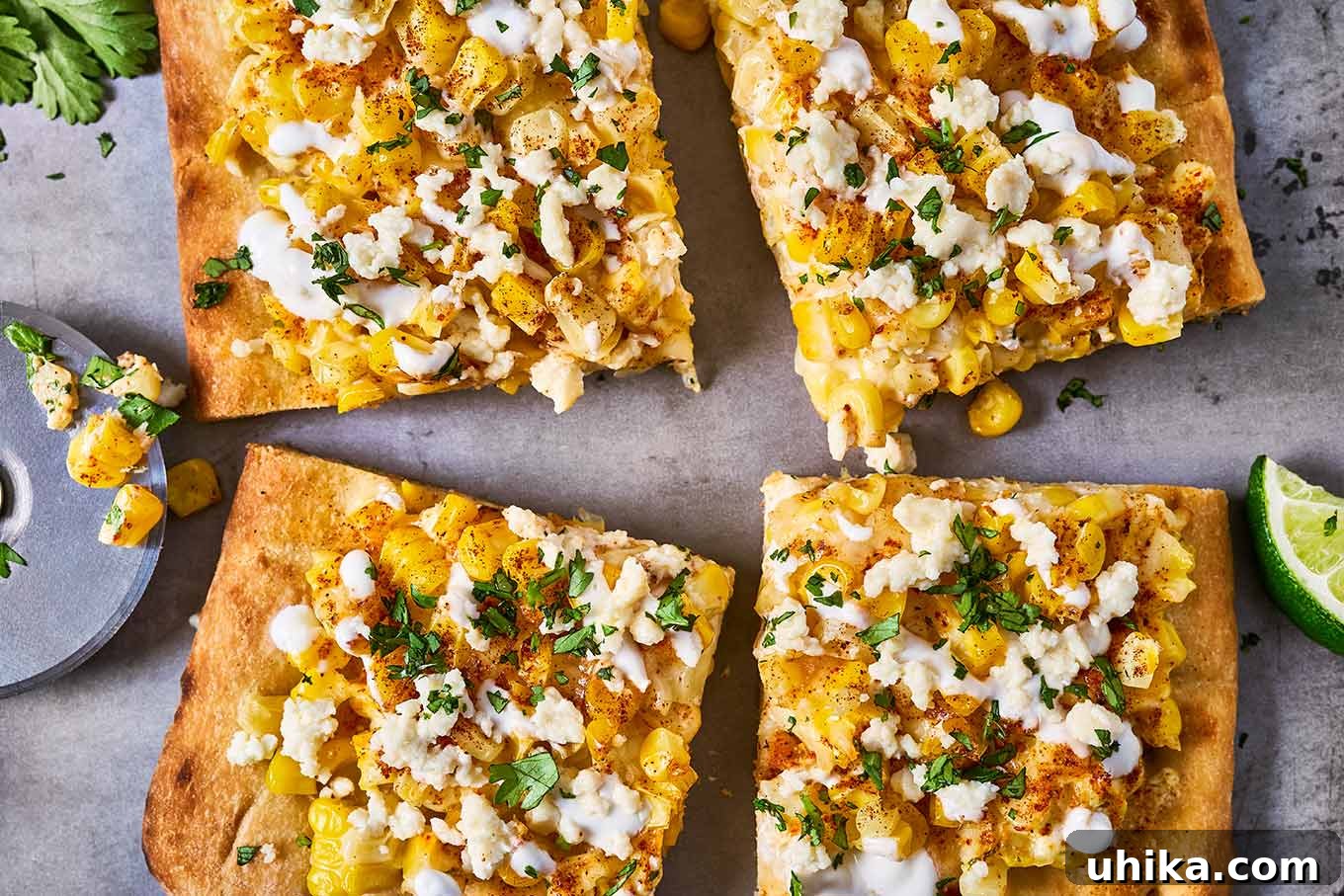 Elote Flatbread Fiesta 6 An inviting overhead view of four perfectly baked and sliced pieces of Mexican street corn flatbread, beautifully drizzled with creamy crema, presented alongside fresh lime wedges, a convenient pizza cutter, and a sprig of vibrant cilantro, ready to be enjoyed.
