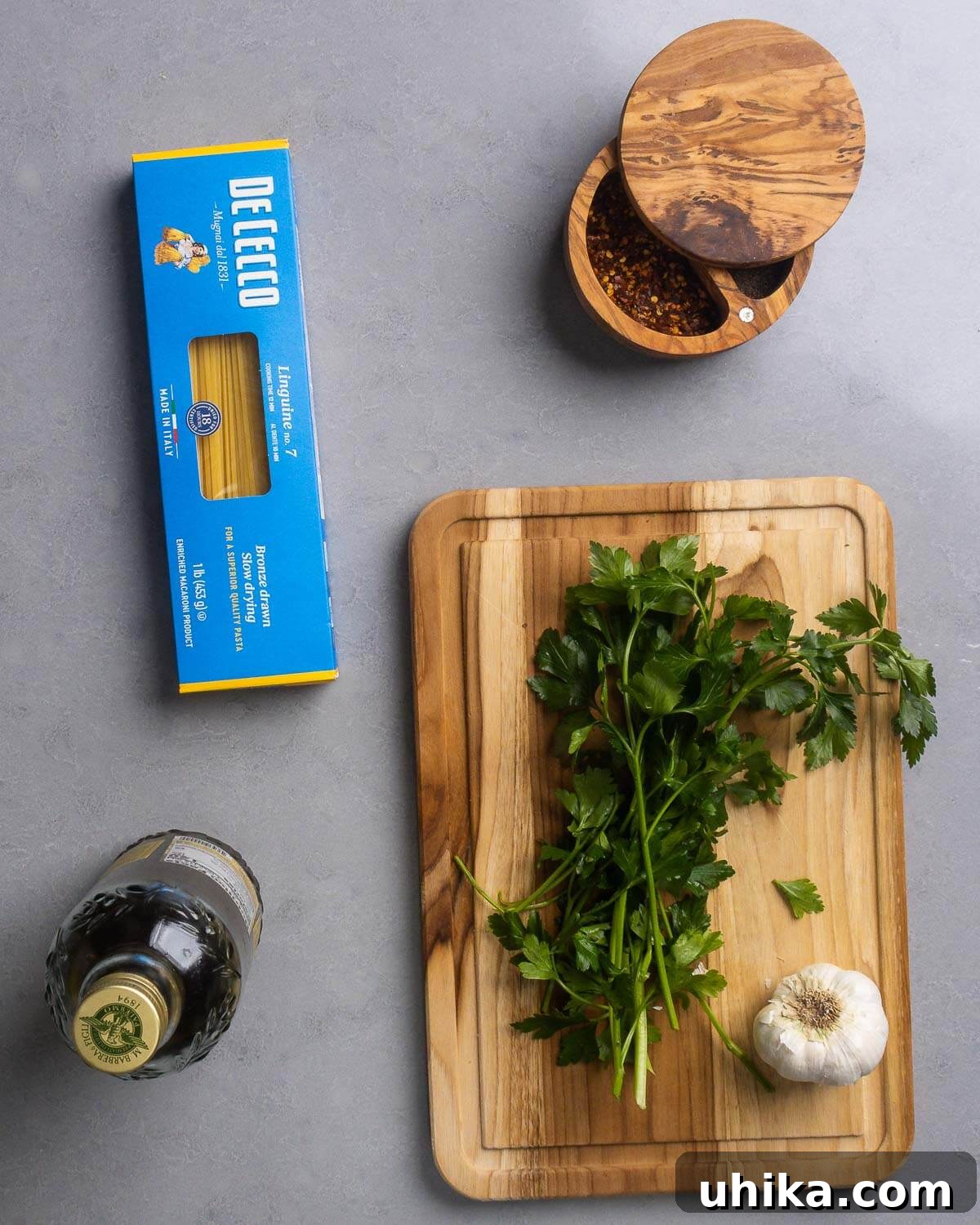 Aromatic Garlic and Olive Oil Linguine 3 A flat lay of Linguine Aglio e Olio ingredients: a box of linguine pasta, red pepper flakes, a bottle of extra virgin olive oil, fresh flat-leaf Italian parsley, and whole garlic cloves.