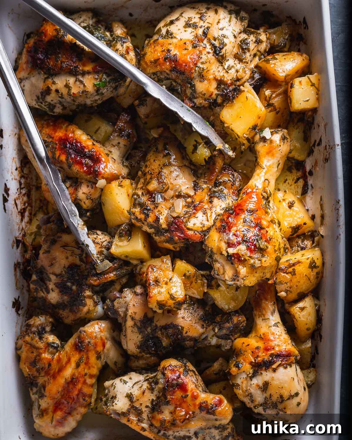 Garlic Rosemary Chicken and Roasted Potatoes 5 Overhead shot of a white baking dish filled with perfectly baked Italian chicken and golden roasted potatoes, with serving tongs hovering over the dish.