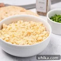 Fresh, homemade breadcrumbs in a bowl with a slice of bread, a prep bowl of chopped parsley, a bread knife, and some seasoning in the background.