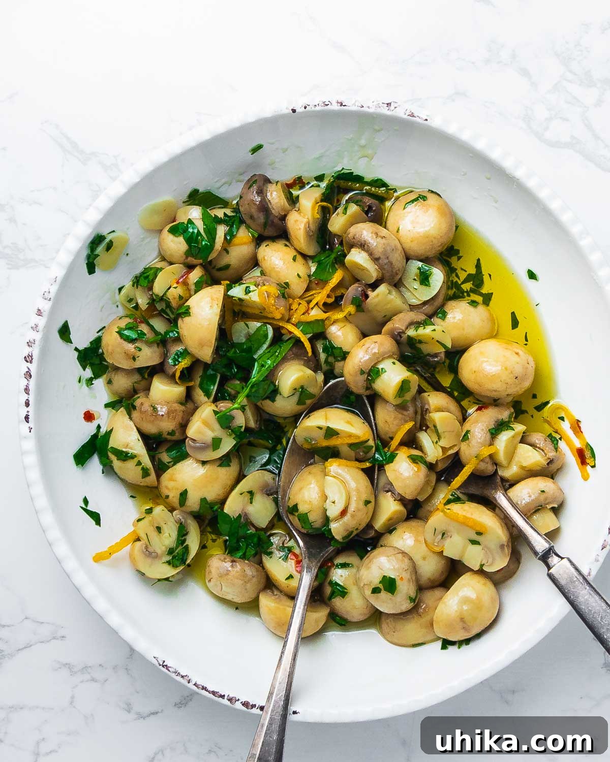 Flavor Infused Mushrooms 6 Overhead shot of plated marinated mushrooms garnished with fresh parsley and olive oil on a marble countertop.