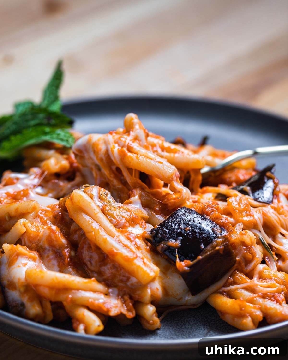 A grey plate featuring a generous serving of Pasta alla Siciliana, garnished with fresh mint, and accompanied by a fork.