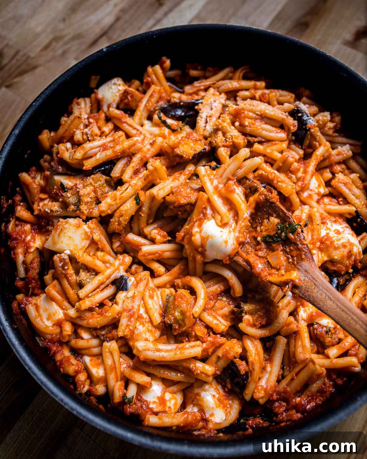 Casarecce pasta with roasted eggplant and melted mozzarella, tossed in a rich tomato sauce, shown in a large pan.