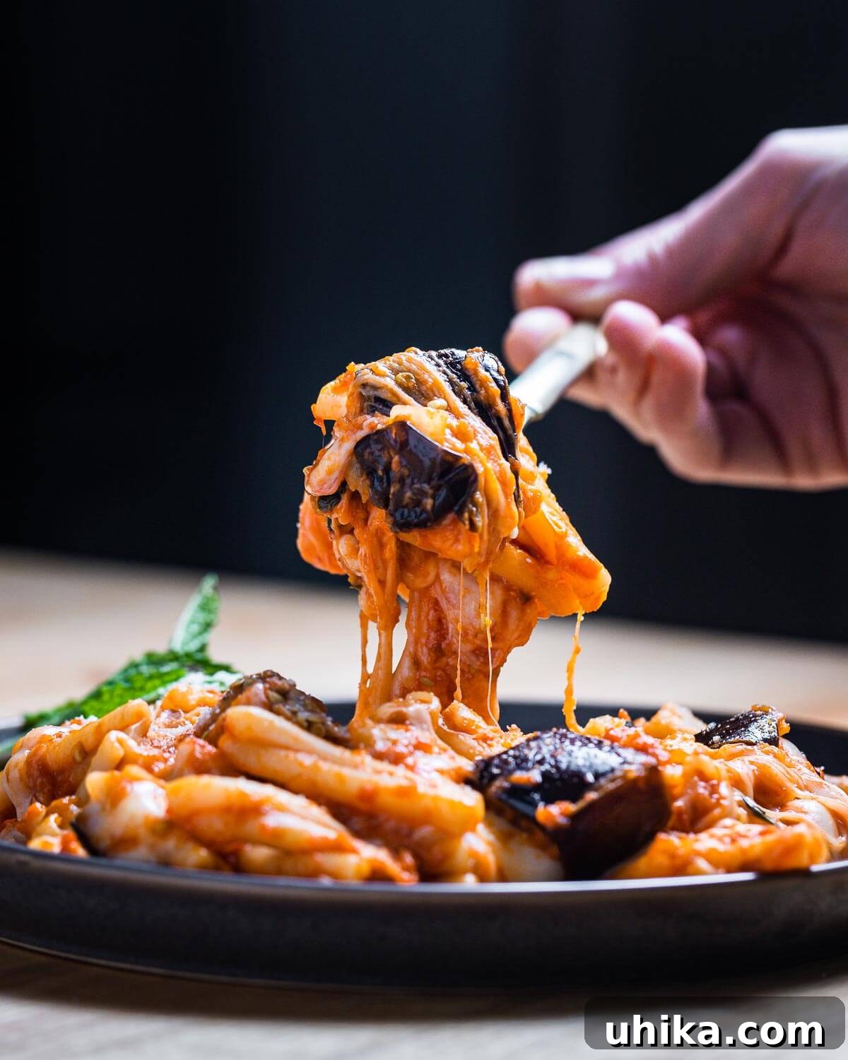 A fork holding a bite of casarecce pasta, eggplant, and mozzarella above a plate of Pasta alla Siciliana, ready to be enjoyed.