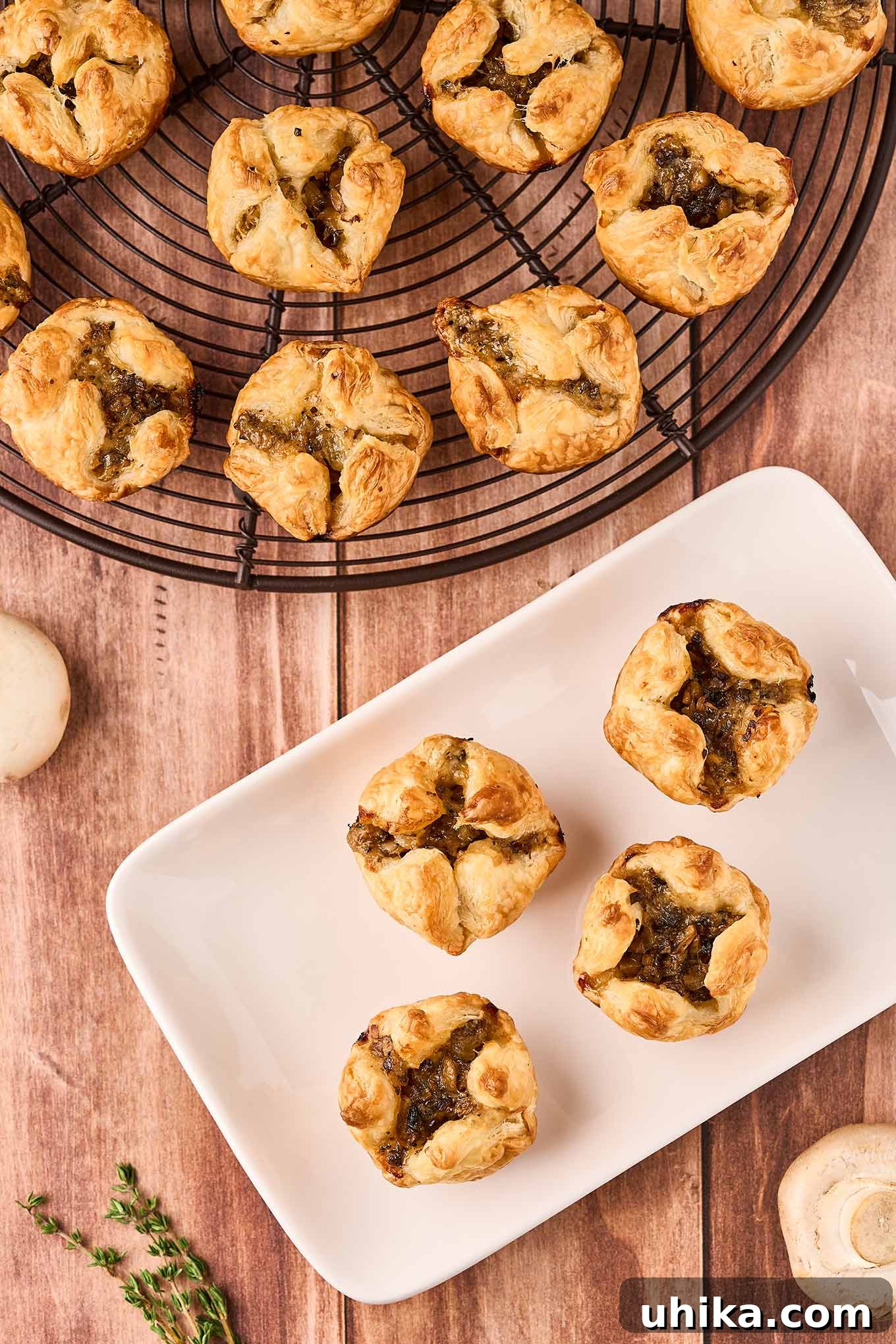 Umami Cloudlets 2 An overhead view of mushroom puff pastry appetizers on a cooling rack next to a small serving plate with four mushroom puffs on it.