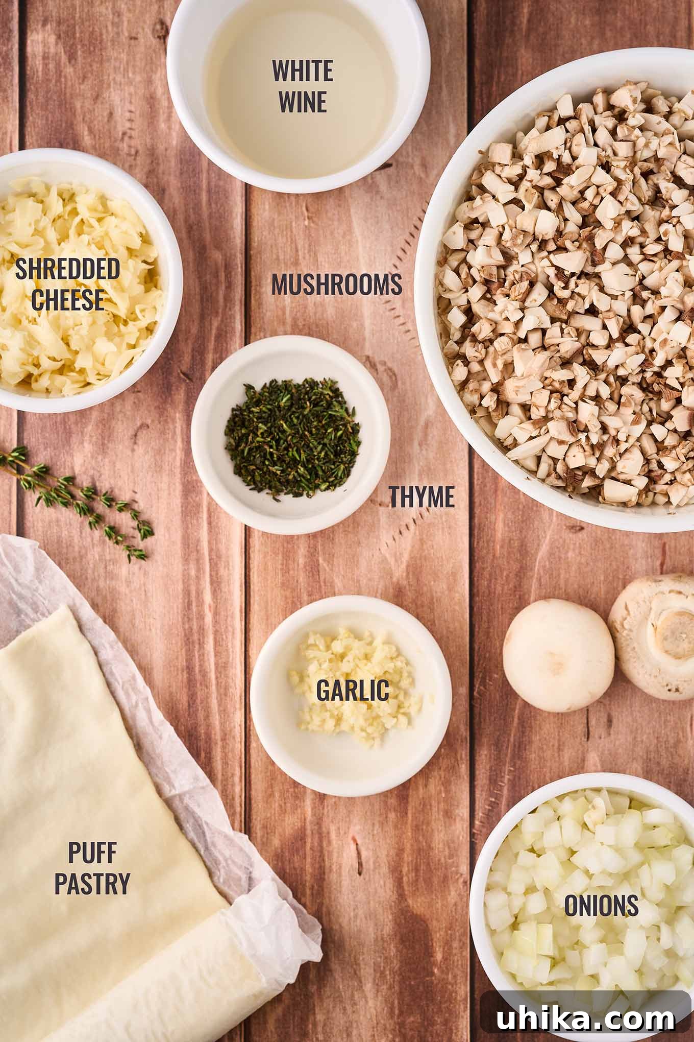Umami Cloudlets 3 A labeled, overhead view of the ingredients for mushroom puffs including pastry dough, mushrooms, onions, garlic, thyme, shredded cheese, and white wine.