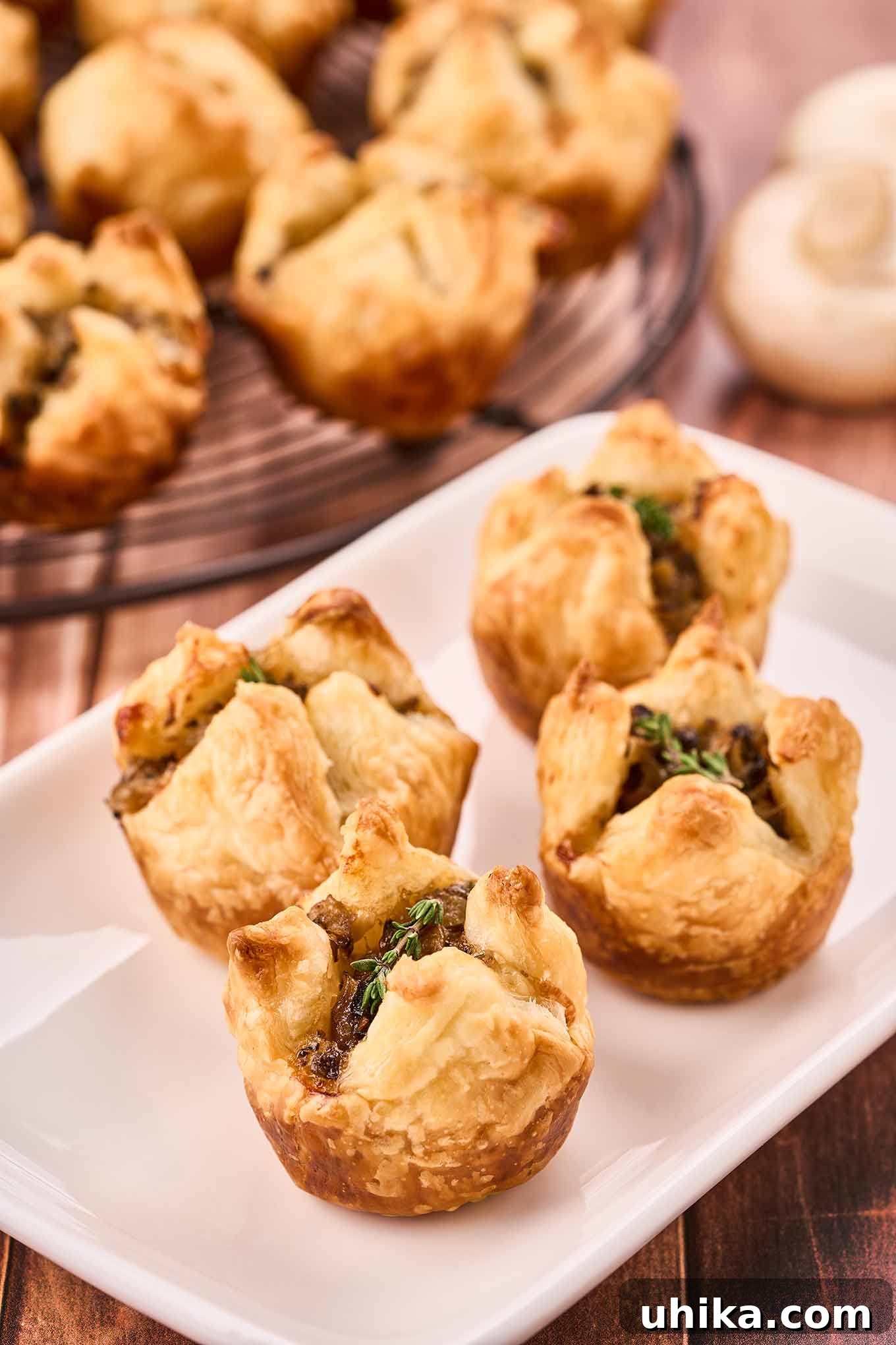 Umami Cloudlets 4 A close-up of mushroom puffs garnished with fresh thyme on an appetizer plate, more in the background.