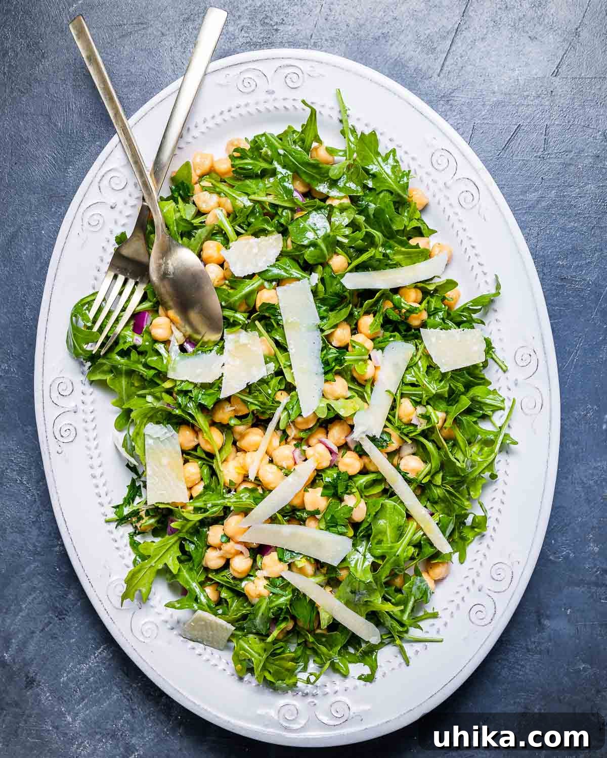 Zesty Lemon Parmesan Chickpea Arugula Salad 6 An overhead shot of the finished chickpea arugula salad on a white platter with shaved cheese, placed on a rustic blue board.