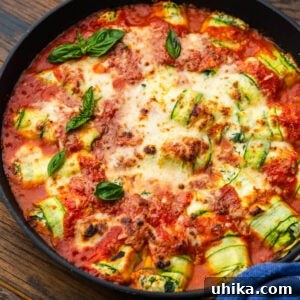 Zucchini rollatini arranged neatly in a baking dish, topped with sauce and cheese before baking.