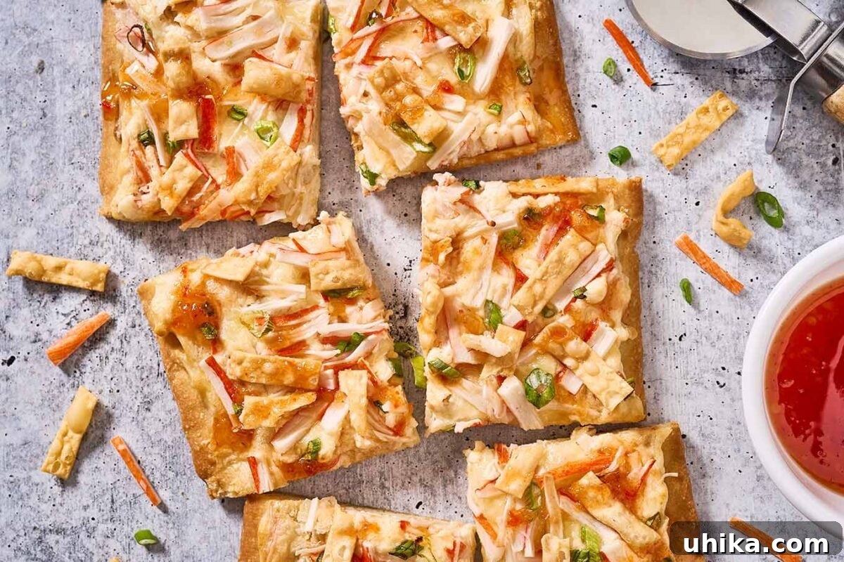 Creamy Crab Rangoon Pizza 8 Squares of crab Rangoon flatbread on a gray surface surrounded by a pizza cutter, dipping bowl of sweet Thai chili sauce, and bits of ingredients.