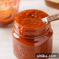 Handcrafted Bourbon BBQ Delight 3 A small jar of rich, homemade bourbon barbecue sauce with a wooden-handled spoon, measuring cup, and a bottle of bourbon in the background.