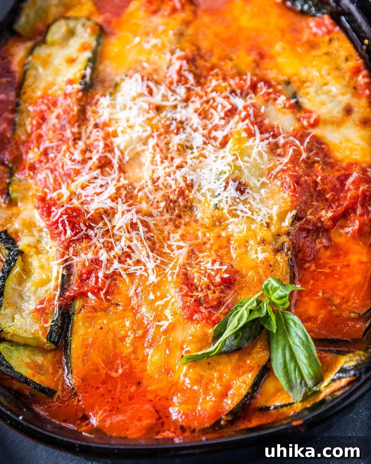 Golden, bubbly zucchini parmigiana in a black baking dish, garnished with fresh basil leaves.