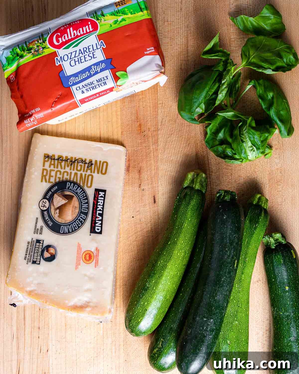 Ingredients for Zucchini alla Parmigiana: fresh mozzarella, basil, Parmigiano Reggiano block, and four fresh zucchinis.